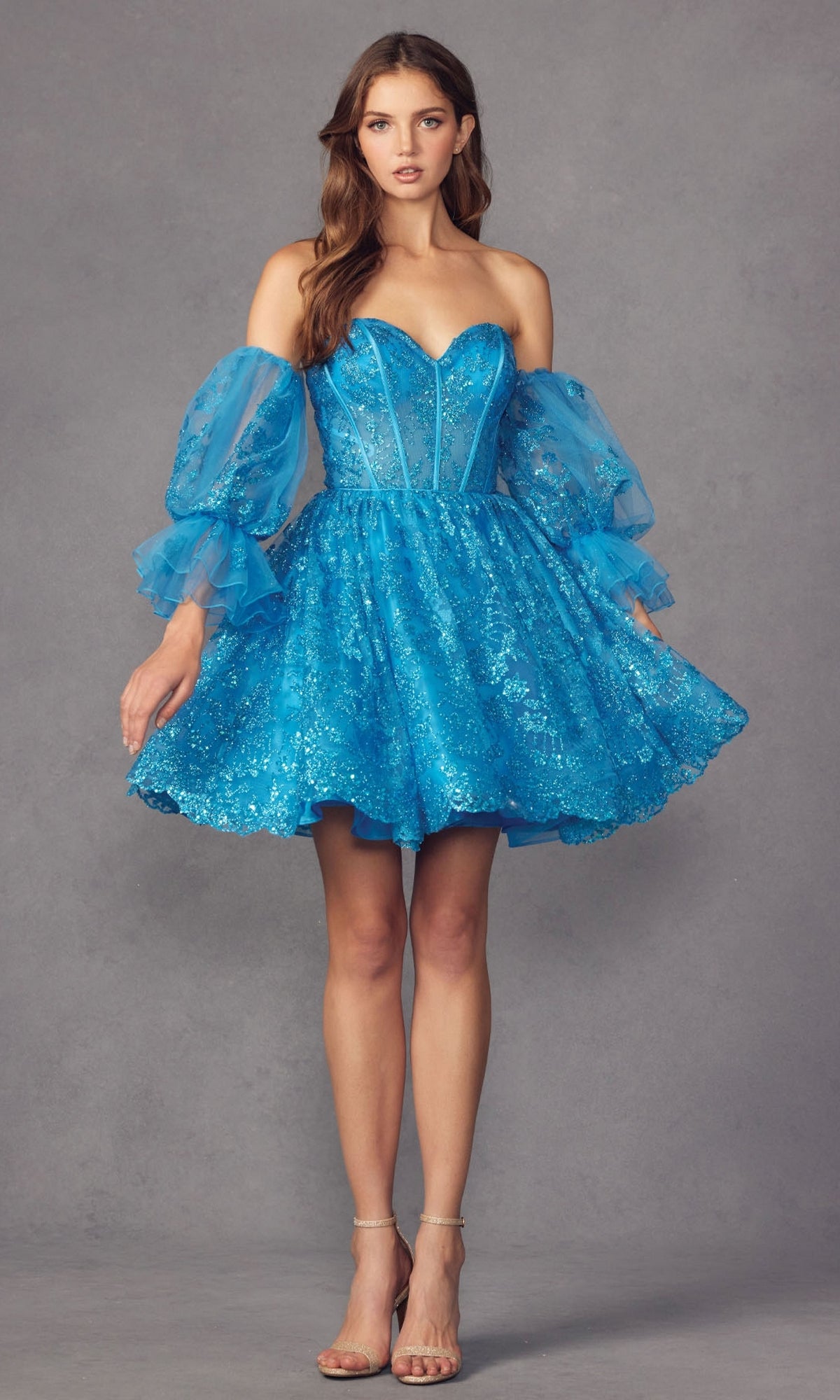 A woman wears the Puff-Sleeve Short Strapless A-Line Prom Dress 895 with removable puff sleeves and transparent heels, standing against a gray background.